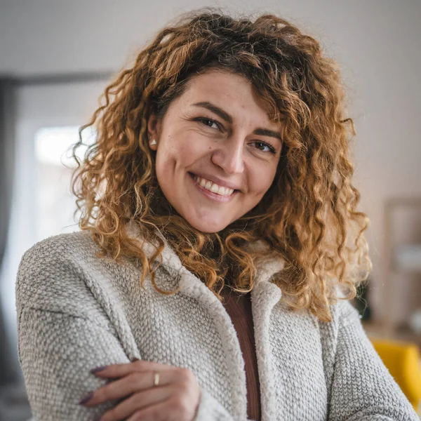 Evde kıvırcık saçlı, mutlu gülümseyen yetişkin beyaz kadın portresi.