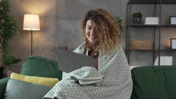一个头发卷曲的高加索女人坐在家里用数码平板电脑看电影或在线连续剧 或者有视频叫快乐微笑 享受慢动作的快乐时光 — 图库视频影像