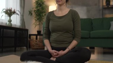 Yetişkin bir kadın Kafkas kadın milenyumu kulaklıkları online rehberli meditasyon için kullanıyor evde gözleri kapalı farkındalık yogası yapıyor gerçek insanlar özbakım kavramı yavaş çekim
