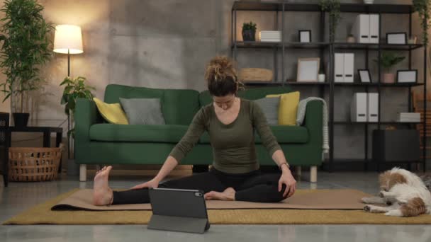 女人在家里客厅的垫子上练习瑜伽 用数码平板电脑进行网上速度慢动作训练 — 图库视频影像