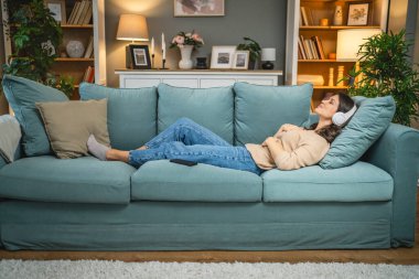 Yetişkin bir kadın Kafkas kadın milenyumu kulaklıkları internet rehberli meditasyon için kullanıyor evde farkındalık yogası uyguluyor gerçek insanlar kişisel bakım kavramını kopyalıyor.