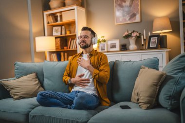 Kulaklıklı bir adam evde yoga eğitimi alıyor.