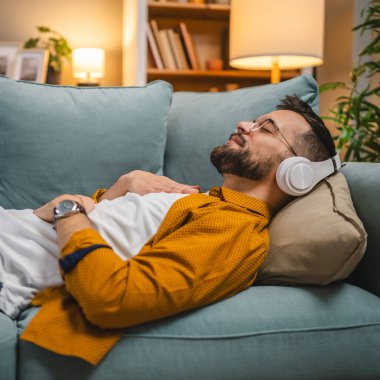 Kulaklıklı bir adam evde yoga eğitimi alıyor.