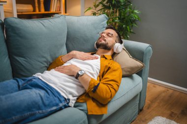 Kulaklıklı bir adam evde yoga eğitimi alıyor.