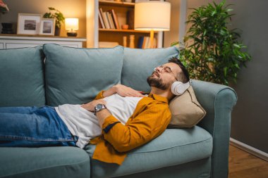 Kulaklıklı bir adam evde yoga eğitimi alıyor.