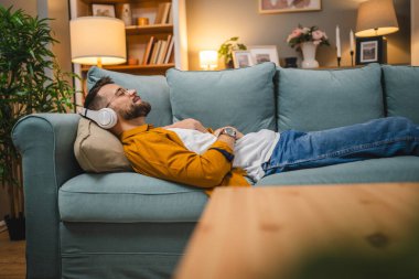 Kulaklıklı bir adam evde yoga eğitimi alıyor.