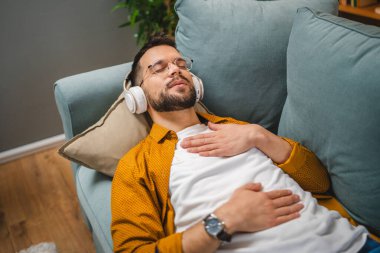 Kulaklıklı bir adam evde yoga eğitimi alıyor.