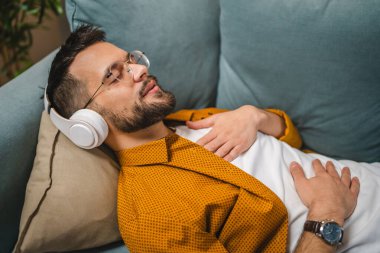 Kulaklıklı bir adam evde yoga eğitimi alıyor.