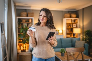 Evde mutlu gülümseyen yetişkin bir kadın banka kartı ve dijital tablet alışverişi e-bankacılık konseptini tutuyor. Gerçek insanlar uzay e-ticaretini kopyalıyor ya da rezervasyon yaptırıyor.