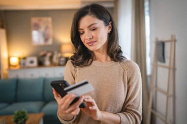 Evde mutlu gülümseyen yetişkin bir kadın banka kartı ve dijital tablet alışverişi e-bankacılık konseptini tutuyor. Gerçek insanlar uzay e-ticaretini kopyalıyor ya da rezervasyon yaptırıyor.