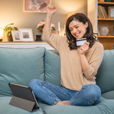 Evde mutlu gülümseyen yetişkin bir kadın banka kartı ve dijital tablet alışverişi e-bankacılık konseptini tutuyor. Gerçek insanlar uzay e-ticaretini kopyalıyor ya da rezervasyon yaptırıyor.