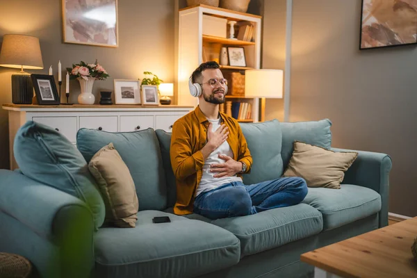 Kulaklıklı bir adam evde yoga eğitimi alıyor.