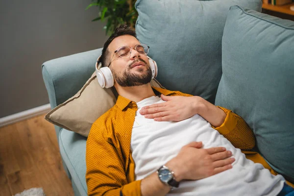 Kulaklıklı bir adam evde yoga eğitimi alıyor.