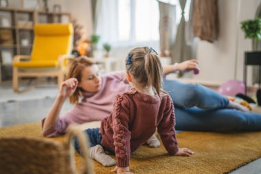 Anne ve kız çocuğu evde, odada yerde oynuyorlar.