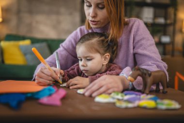 Anne ve kızı yeni yürümeye başlayan çocuk odada el sanatlarında oynuyorlar.