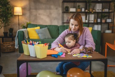 Anne ve kızı yeni yürümeye başlayan çocuk odada el sanatlarında oynuyorlar.
