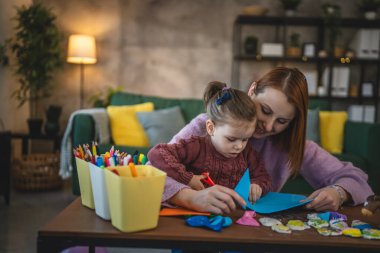Anne ve kızı yeni yürümeye başlayan çocuk odada el sanatlarında oynuyorlar.
