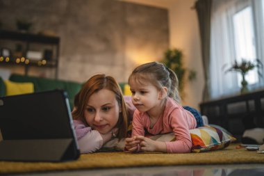 Anne ve kızı evde online video izlemek için dijital tablet kullanıyorlar.
