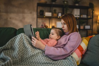 Anne ve kızı evde online video izlemek için dijital tablet kullanıyorlar.