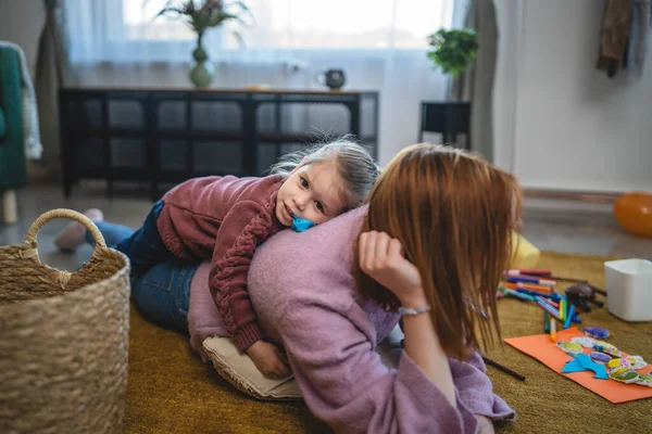 Anne ve kız çocuğu evde, odada yerde oynuyorlar.