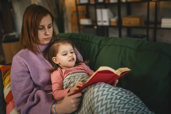 Anne ve kız bebek evde kitap okuyorlar.
