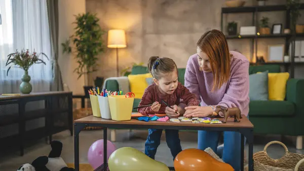 Anne ve kızı yeni yürümeye başlayan çocuk odada el sanatlarında oynuyorlar.