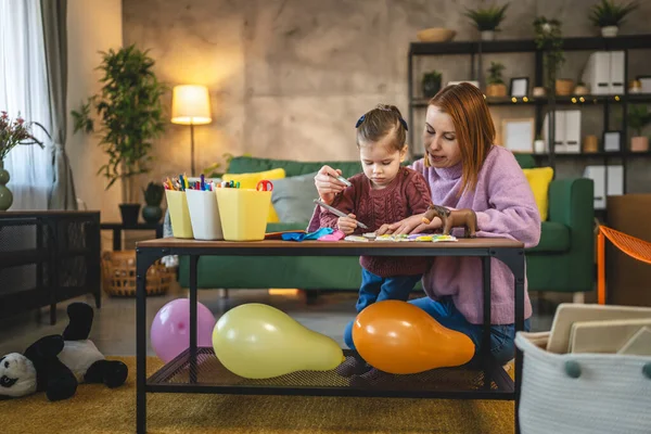 Anne ve kızı yeni yürümeye başlayan çocuk odada el sanatlarında oynuyorlar.