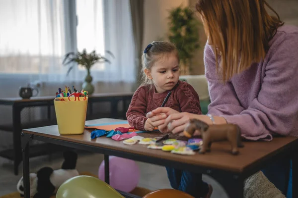 Anne ve kızı yeni yürümeye başlayan çocuk odada el sanatlarında oynuyorlar.