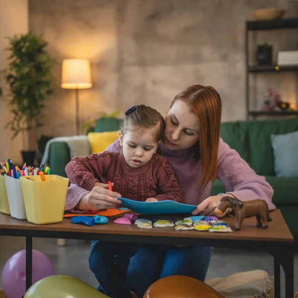 Anne ve kızı yeni yürümeye başlayan çocuk odada el sanatlarında oynuyorlar.
