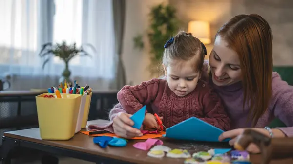 Anne ve kızı yeni yürümeye başlayan çocuk odada el sanatlarında oynuyorlar.