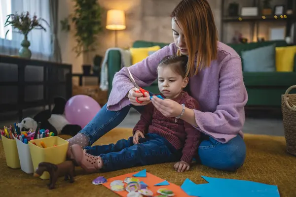 Anne ve kızı yeni yürümeye başlayan çocuk odada el sanatlarında oynuyorlar.