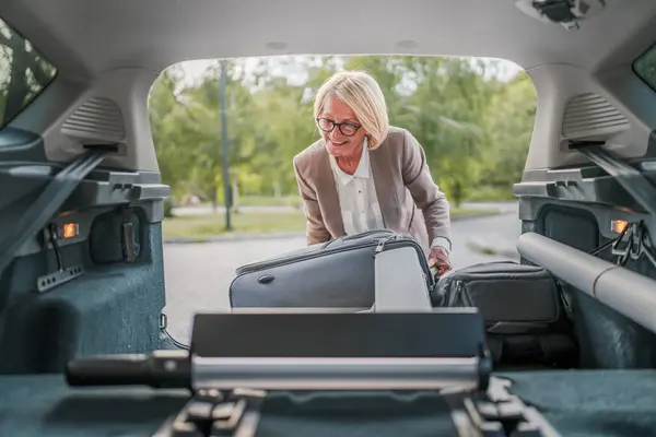 Olgun, sarışın, güzel bir iş kadını seyahat konsepti. Kadın, taşınırken ya da varış noktasına varırken arabasının bagajından eşyalarını alır. Ya da işe giderken gerçek insanlar mekanı kopyalarlar.