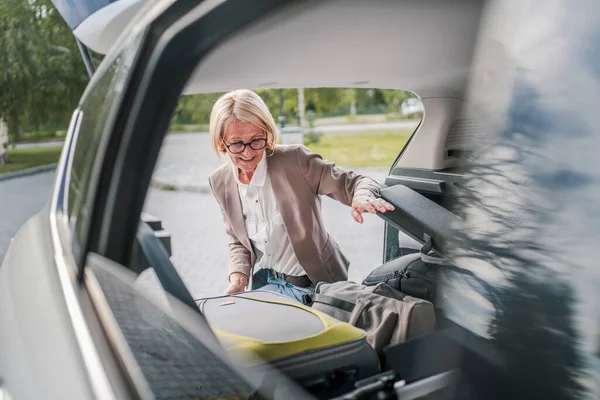 Olgun, sarışın, güzel bir iş kadını seyahat konsepti. Kadın, taşınırken ya da varış noktasına varırken arabasının bagajından eşyalarını alır. Ya da işe giderken gerçek insanlar mekanı kopyalarlar.