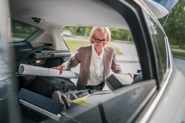 Olgun, sarışın, güzel bir iş kadını seyahat konsepti. Kadın, taşınırken ya da varış noktasına varırken arabasının bagajından eşyalarını alır. Ya da işe giderken gerçek insanlar mekanı kopyalarlar.