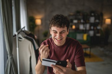 Genç bir beyaz erkek evde oturuyor. İnternet üzerinden kredi kartı alışverişi yapıyor. İnternetten modern elektronik bankacılık satın alıyor.