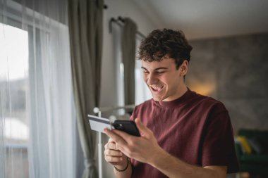 Genç bir beyaz erkek evde oturuyor. İnternet üzerinden kredi kartı alışverişi yapıyor. İnternetten modern elektronik bankacılık satın alıyor.