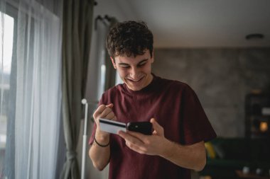 Genç bir beyaz erkek evde oturuyor. İnternet üzerinden kredi kartı alışverişi yapıyor. İnternetten modern elektronik bankacılık satın alıyor.