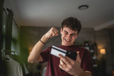 Genç bir beyaz erkek evde oturuyor. İnternet üzerinden kredi kartı alışverişi yapıyor. İnternetten modern elektronik bankacılık satın alıyor.