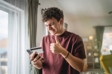 Genç bir beyaz erkek evde oturuyor. İnternet üzerinden kredi kartı alışverişi yapıyor. İnternetten modern elektronik bankacılık satın alıyor.