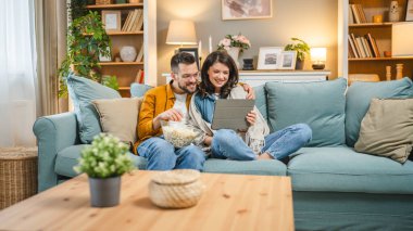 Kafkasyalı erkek ve kadın, karı-koca ya da erkek arkadaş ya da kız arkadaş evde film serisi kanepede oturup patlamış mısırlı mutlu bir gülümsemeyle aşk aile kavramını kopyalayan mutlu bir gülümseme.