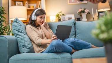 Yetişkin bir kadın beyaz kadın evde film videosu izlerken kanepeye oturur dijital tablet kullanır ya da video görüşmesi yapar.