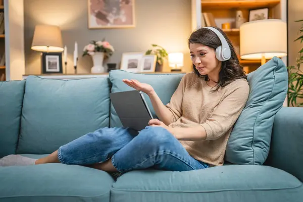 Yetişkin bir kadın beyaz kadın evde film videosu izlerken kanepeye oturur dijital tablet kullanır ya da video görüşmesi yapar.