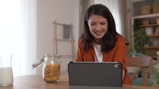 1人の白人女性が自宅で座ってデジタルタブレットを使用して ビデオコールハッピー笑顔を持って楽しい時間のスローモーション毎日のルーチンを持っています — ストック動画