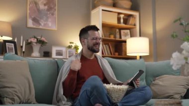 Bir yetişkin erkek beyaz erkek, evdeki film videosunun çekyatında dijital tablet kullanıyor.