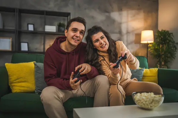 大人のカップル男性と女性の慎重な夫と妻またはボーイフレンドとガールフレンドは 自宅でコンソールビデオゲームをプレイするジョイスティックコントローラーは楽しいレジャーの喜びと絆の概念を持っています — ストック写真