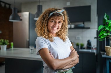 Kıvırcık saçlı yetişkin bir kadının yakın portresi mutlu bir gülümseme olumlu duygu fotokopi alanı evde duruyor.