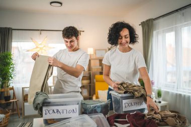 Anne ve oğul evlerinde durup bağış için kıyafet seçiyorlar. Genç, deli ve beyaz kadınlar evlerinin oturma odasındaki kutulara gardırop düzenliyorlar.