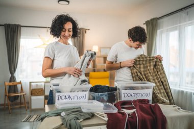 Anne ve oğul evlerinde durup bağış için kıyafet seçiyorlar. Genç, deli ve beyaz kadınlar evlerinin oturma odasındaki kutulara gardırop düzenliyorlar.
