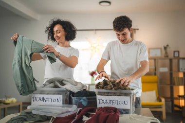 Anne ve oğul evlerinde durup bağış için kıyafet seçiyorlar. Genç, deli ve beyaz kadınlar evlerinin oturma odasındaki kutulara gardırop düzenliyorlar.