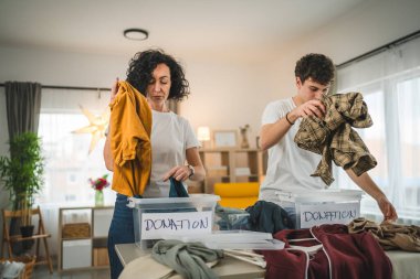 Anne ve oğul evlerinde durup bağış için kıyafet seçiyorlar. Genç, deli ve beyaz kadınlar evlerinin oturma odasındaki kutulara gardırop düzenliyorlar.